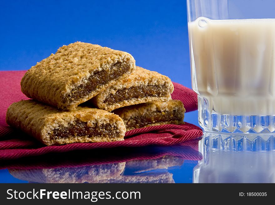Wheat fig bars on red cloth napkin with glass of milk on blue background. Wheat fig bars on red cloth napkin with glass of milk on blue background