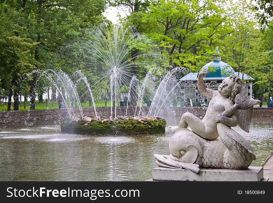 Sculpture of naked boy sitting on background in lower park of Peterhof. Saint Petersburg. Russia. Sculpture of naked boy sitting on background in lower park of Peterhof. Saint Petersburg. Russia