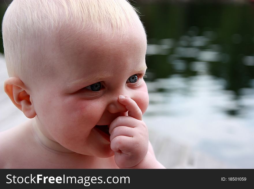 Blond haired, blue eyed baby sitting on dock by lake. Blond haired, blue eyed baby sitting on dock by lake