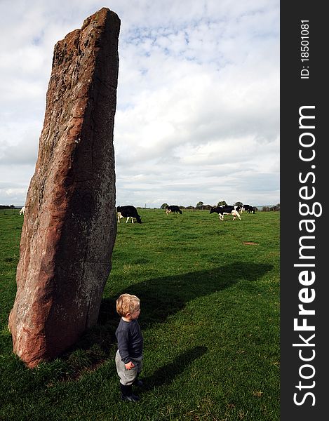 Adorable blond boy standing beside druid's stone, with cows in the background, England. Adorable blond boy standing beside druid's stone, with cows in the background, England.