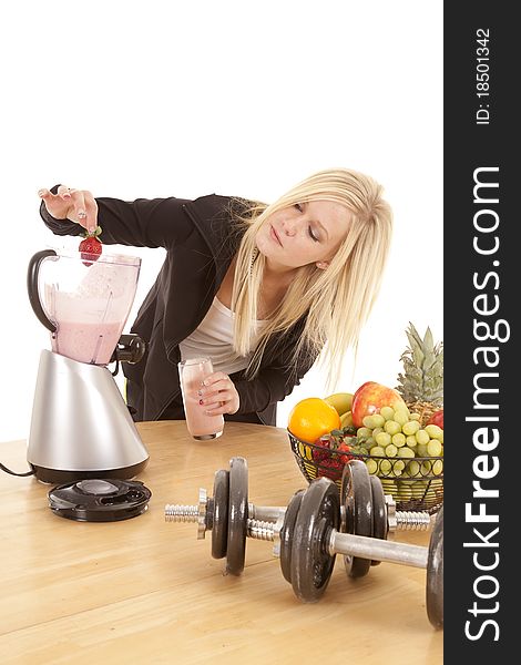 A woman is putting a strawberry into her blender. A woman is putting a strawberry into her blender.