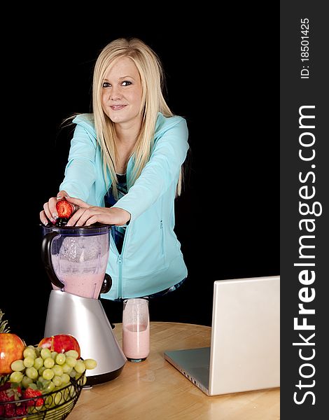 A woman is by a laptop making a smoothie. A woman is by a laptop making a smoothie.