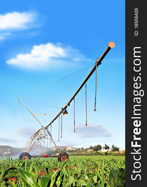 Irrigations system watering a farm field against blue sky