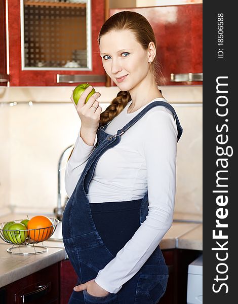 Smiling beautiful pregnant woman at kitchen with apple