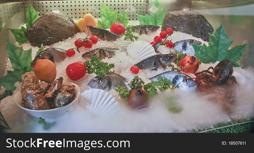 Icy seafood showcase with raw fishes decorated by vegetables and fruits