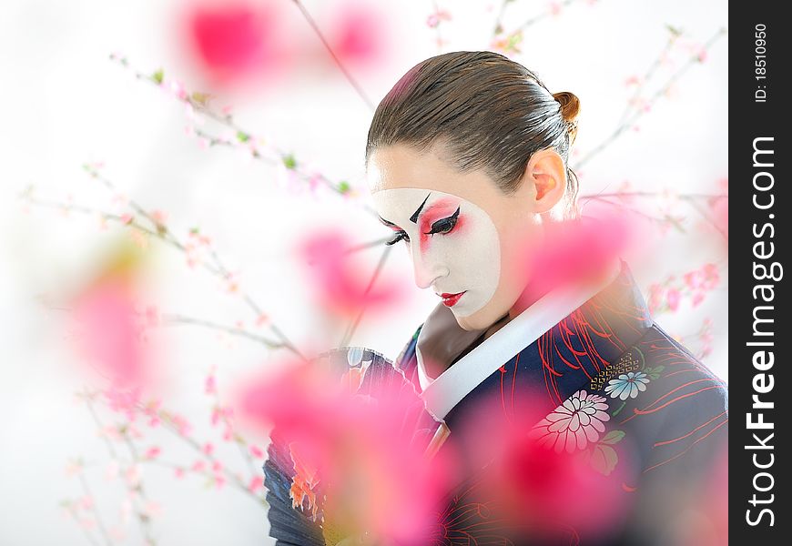 Artistic portrait of japan geisha woman with creative make-up near sakura tree