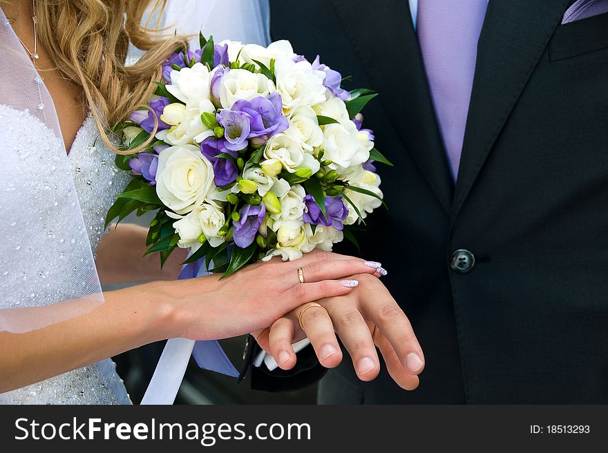 The bride and groom put their hands with rings on the wedding bouquet. The bride and groom put their hands with rings on the wedding bouquet