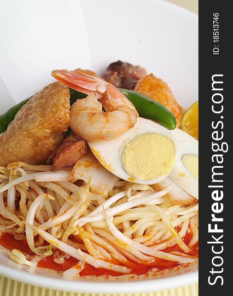 A bowl of curry noodle and garnish with prawn and lime.