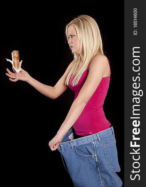 A woman with big pants is looking mad at a donut. A woman with big pants is looking mad at a donut