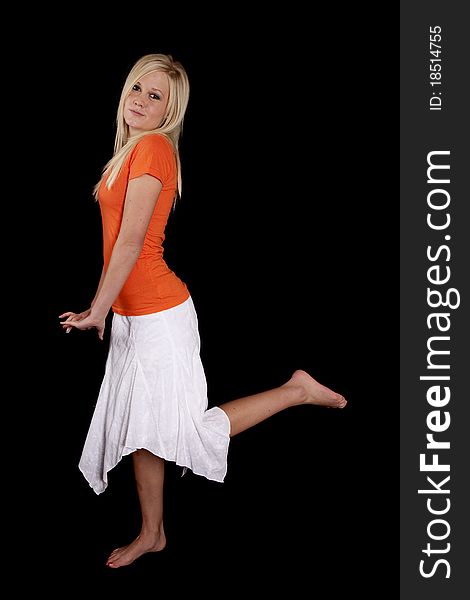 A woman is standing with her leg up wearing an orange shirt and white skirt. A woman is standing with her leg up wearing an orange shirt and white skirt