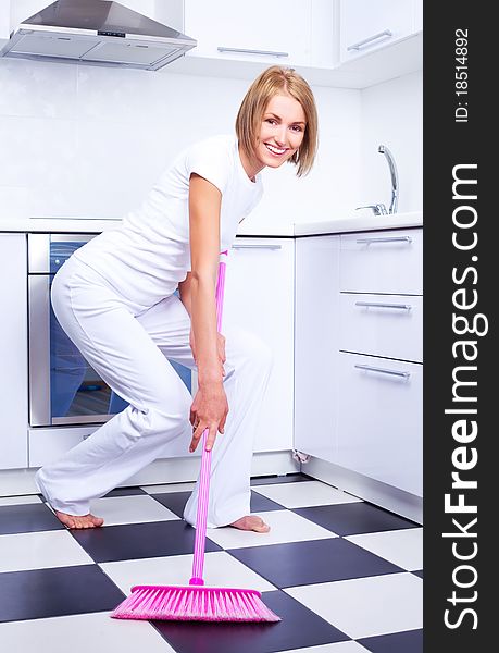 Beautiful young housewife with a broom in the kitchen