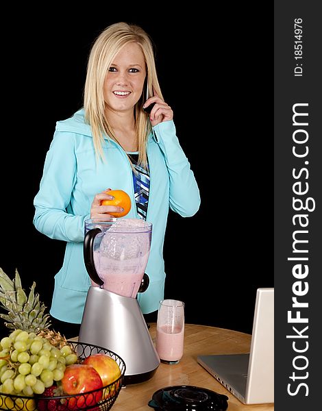 A woman is standing behind a blender on the phone with an orange in her hand. A woman is standing behind a blender on the phone with an orange in her hand.