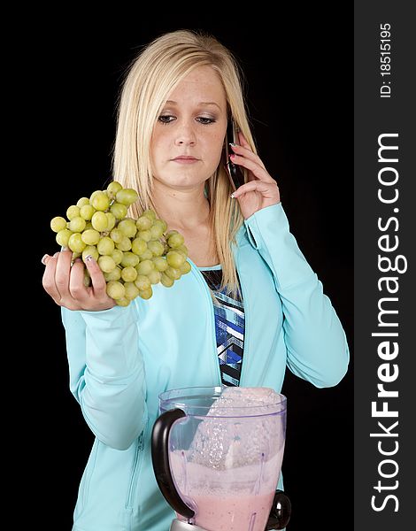 A woman is talking on the phone and making a smoothie holding grapes. A woman is talking on the phone and making a smoothie holding grapes.