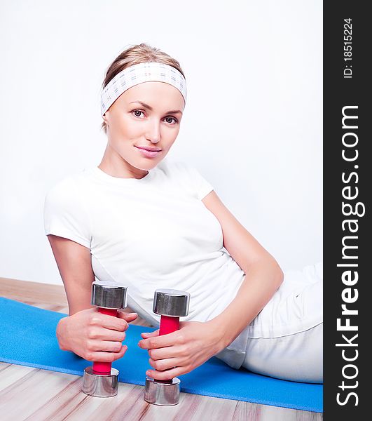 Beautiful young woman on the mat working out with two dumbbells. Beautiful young woman on the mat working out with two dumbbells