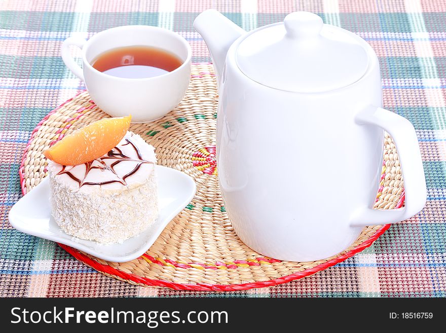 Milk jelly cake with peach and coconut decoration on a white plate, teapot and a cup of tea