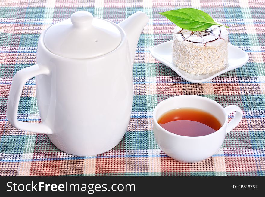 Milk jelly cake with green leaf and coconut decoration on a white plate, teapot and a cup of tea. Milk jelly cake with green leaf and coconut decoration on a white plate, teapot and a cup of tea