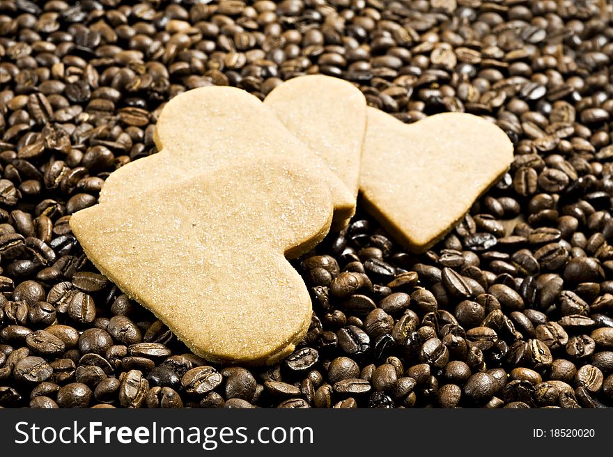 Close up background of a sugar coated heart shaped cookies in coffee beans very shallow depth of field and intentional low light. Close up background of a sugar coated heart shaped cookies in coffee beans very shallow depth of field and intentional low light