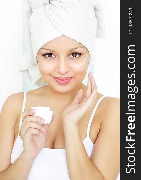 Girl applying cosmetic cream on skin on a light background in room. Girl applying cosmetic cream on skin on a light background in room