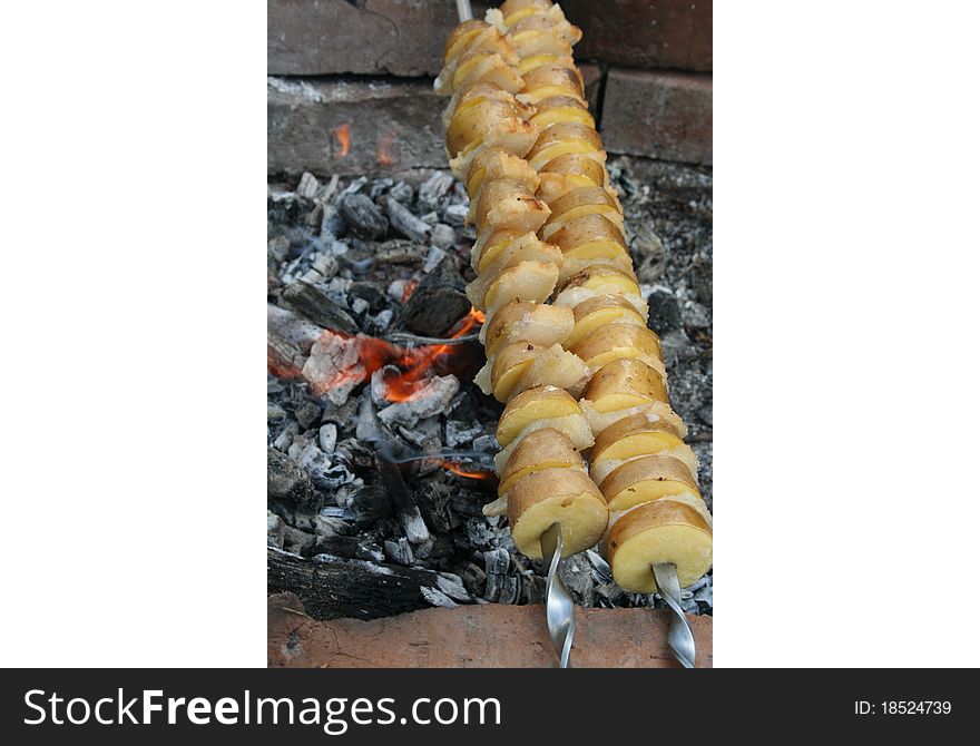 The potato pines on the heated charcoal on skewers with fat slices. The potato pines on the heated charcoal on skewers with fat slices