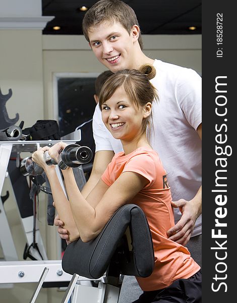 A girl's trainer shows the correct form of exercise with dumbbel. A girl's trainer shows the correct form of exercise with dumbbel