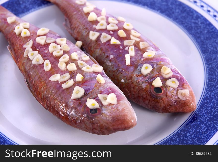 Detail view of two red fish on a plate with garlic on top ready to be made.