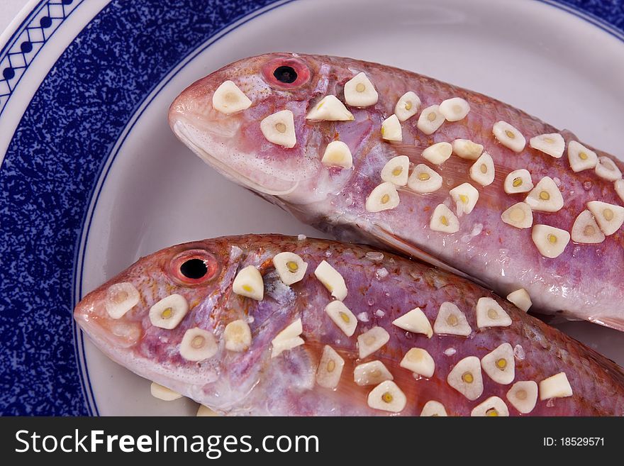 Detail view of two red fish on a plate with garlic on top ready to be made.