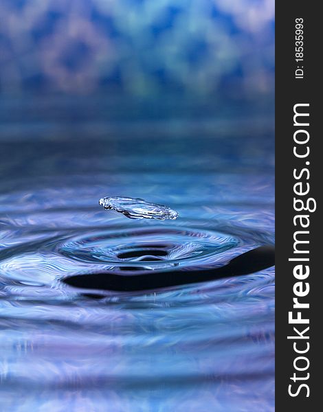 A blue abstract background of a close up of transparent water drops falling in water, making beautifull ripples and flowing waves in the surface and showing the pure energy it creates. Small depth of field.