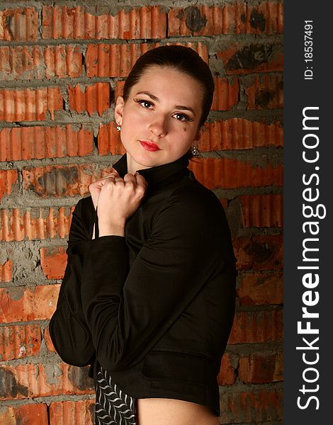 Girl in black suit posing at brickwall.