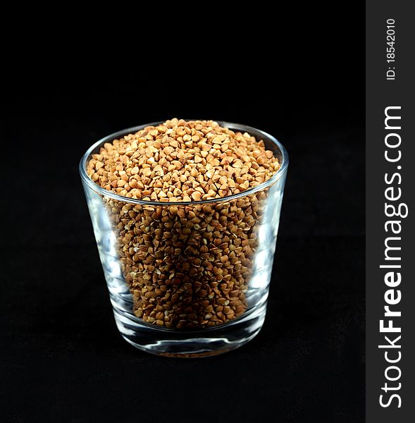 Buckwheat millet kernels in a cup on black background