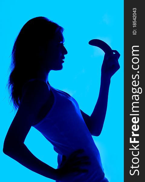 Silhouette of the woman with a banana in a hand on a blue background the isolated