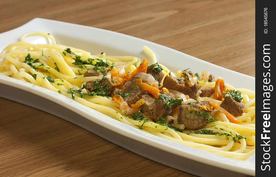 Spaghetti with meat and greens on a long white plate