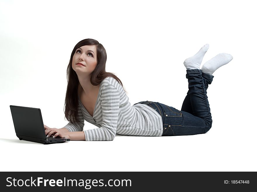 The thoughtful beautiful girl lying on a floor working with the laptop on a white background. The thoughtful beautiful girl lying on a floor working with the laptop on a white background