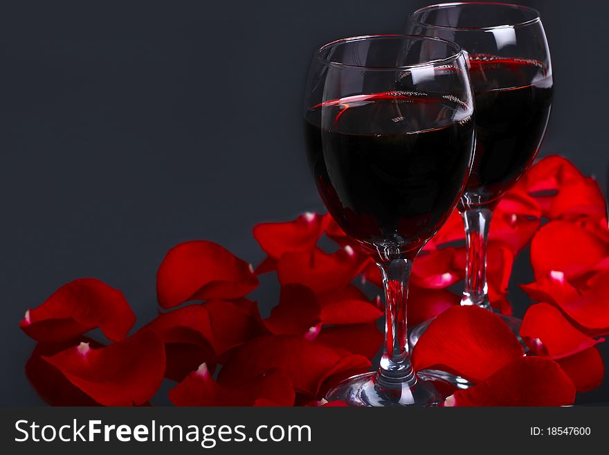 Two glasses of wine with petals of red rose