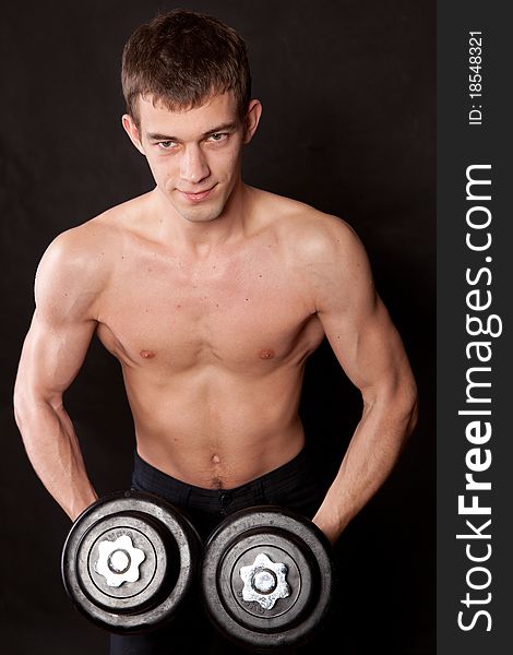Portrait of an energetic naked man lifting dumbbell against black background