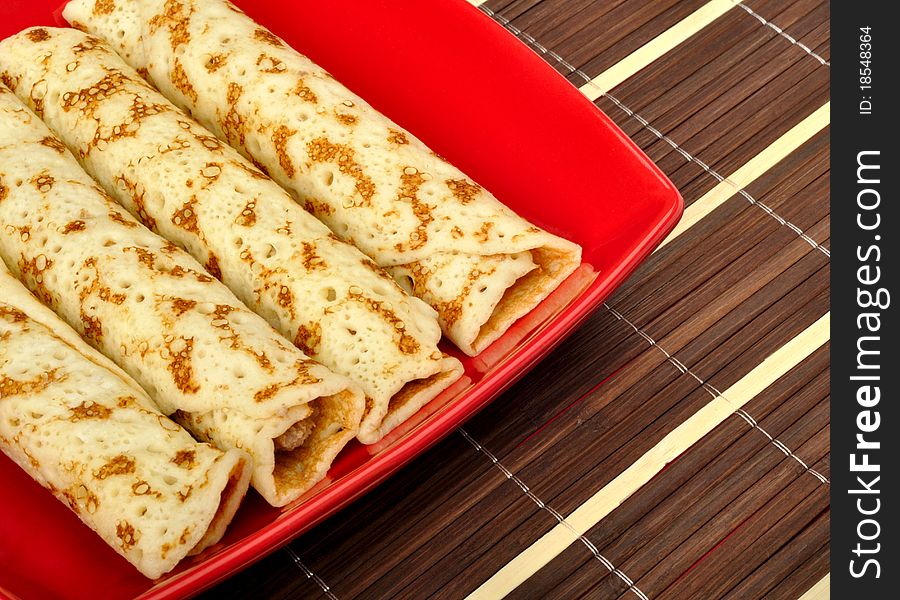 Pancakes in a dish on a wooden mat. Pancakes in a dish on a wooden mat