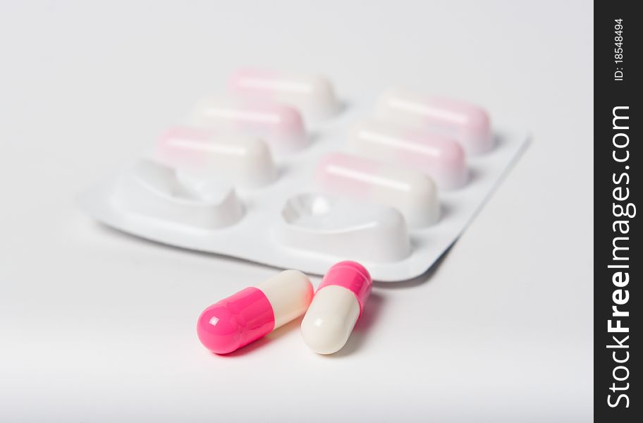 Pink pharmaceutical capsules with packaging close up on white with focus on pills. Pink pharmaceutical capsules with packaging close up on white with focus on pills