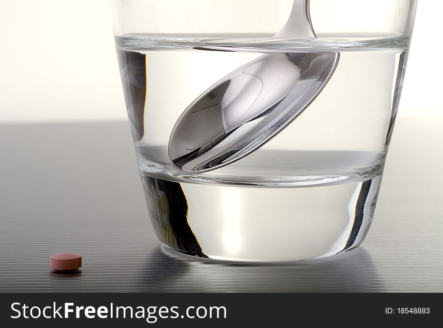 Pill next to a glass of water with a teaspoon