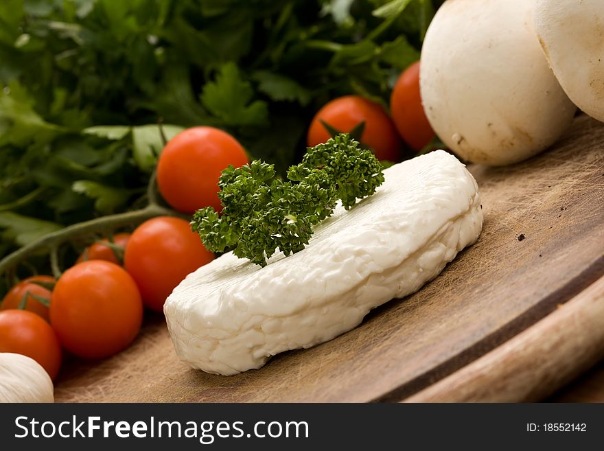 Photo of fresh round ricotta cheese with vegetables arround on wood table