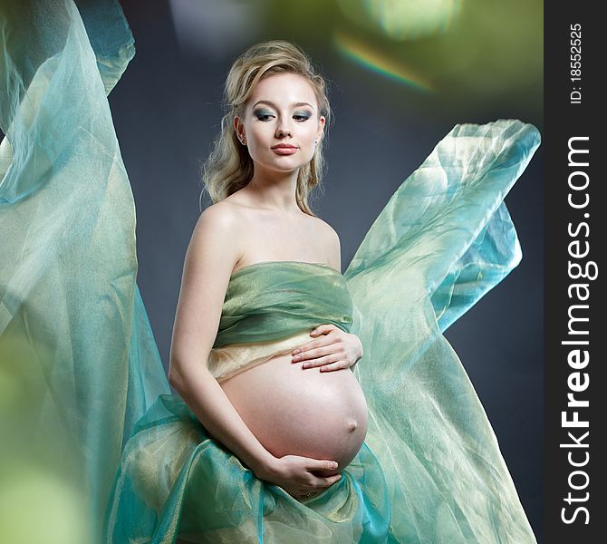 Beautiful pregnant woman in green cloth on grey background
