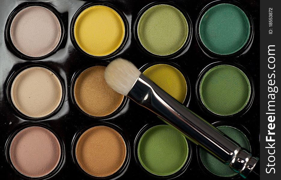 A close-up top view image of a eye-shadow kit, with a professional makeup brush on top of it. A close-up top view image of a eye-shadow kit, with a professional makeup brush on top of it