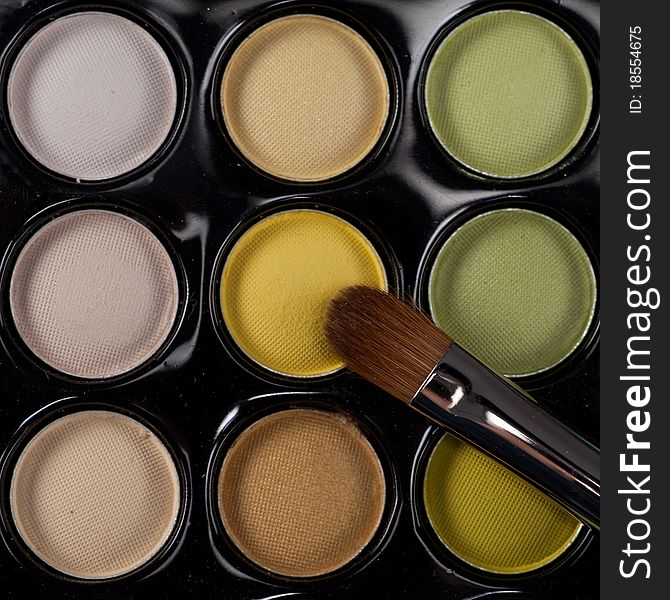 A close-up top view image of a eye-shadow kit, with a professional makeup brush on top of it. A close-up top view image of a eye-shadow kit, with a professional makeup brush on top of it