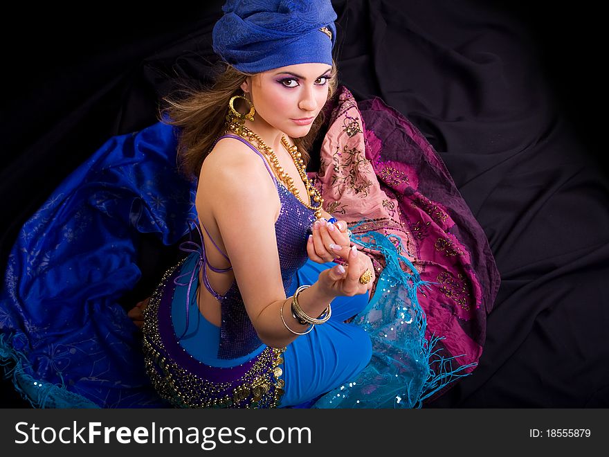 Beautiful girl in a turban and a stylized ethnic costume sits on headscarves