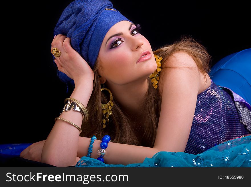 Beautiful girl in a turban and a stylized ethnic costume lies on headscarves