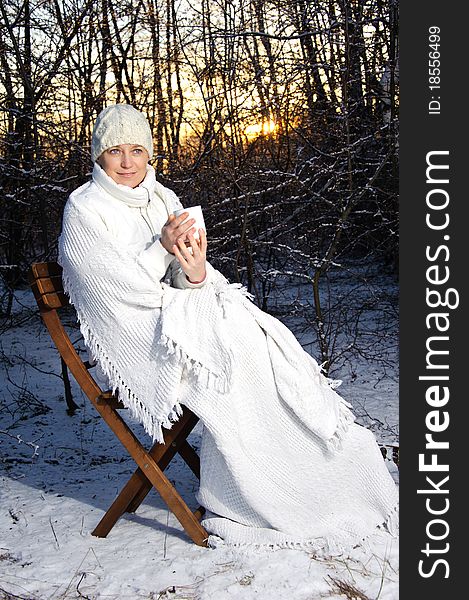 Woman in white, with a mug in his hands, wrapped in a blanket in a winter forest. sunset. Woman in white, with a mug in his hands, wrapped in a blanket in a winter forest. sunset.