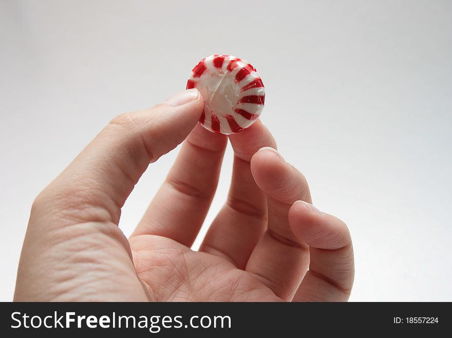 Hand holding a red and white peppermint.