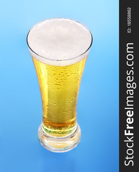 Glass of beer close-up with froth over blue background