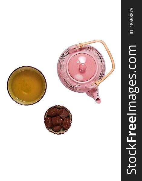 Composition with tea set that shows teakettle, tea in a cup and candies in a bowl on a white background with shadows.