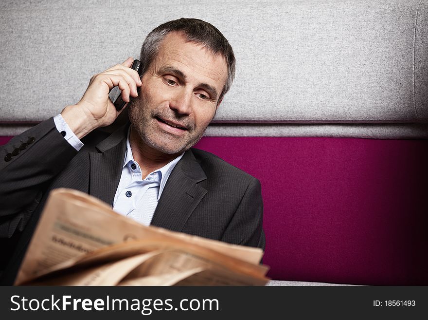 Friendly seniour business executive in grey suit talking on cell phone and reading newspaper. Friendly seniour business executive in grey suit talking on cell phone and reading newspaper.