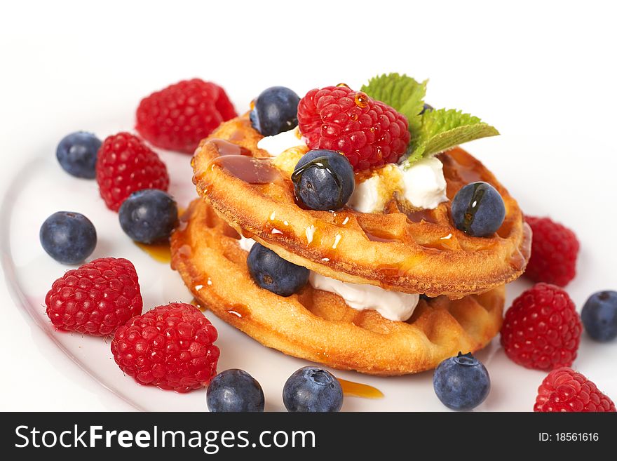 Belgian waffles with fresh raspberries, blueberries, mint leaves and cream on white plate. Belgian waffles with fresh raspberries, blueberries, mint leaves and cream on white plate