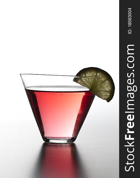 This photograph contains an image of a red alcoholic cocktail with a lemon slice shot on a white background. This photograph contains an image of a red alcoholic cocktail with a lemon slice shot on a white background